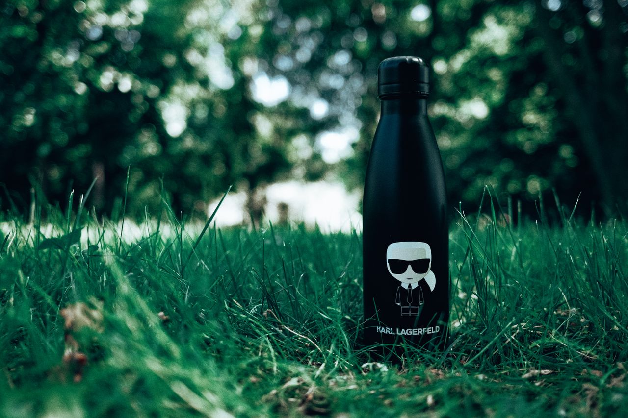 Elegant black water bottle resting on a lush green lawn, encircled by vivid foliage.